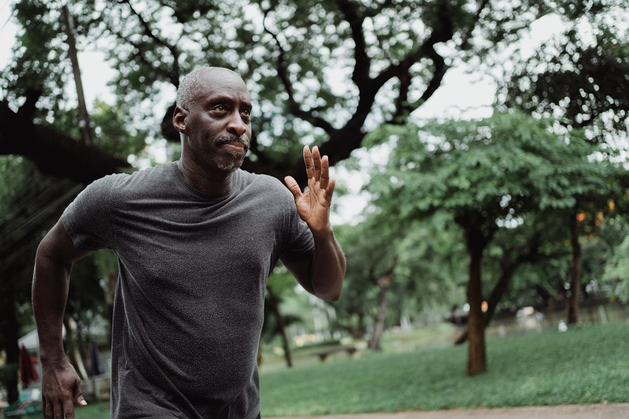 trusted-partner Senior man running through a lush green park, focused on fitness and wellbeing outdoors.